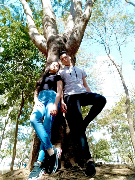 two people pose for the camera underneath a huge tree