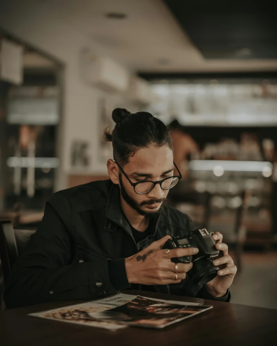 a man wearing glasses sits at a table and uses a camera