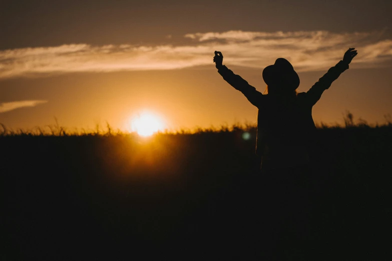 the sun setting behind a person standing in a field with their arms up