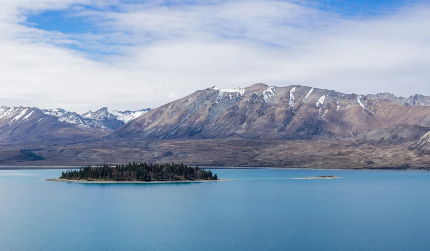 an island in the middle of the ocean with mountains in the background