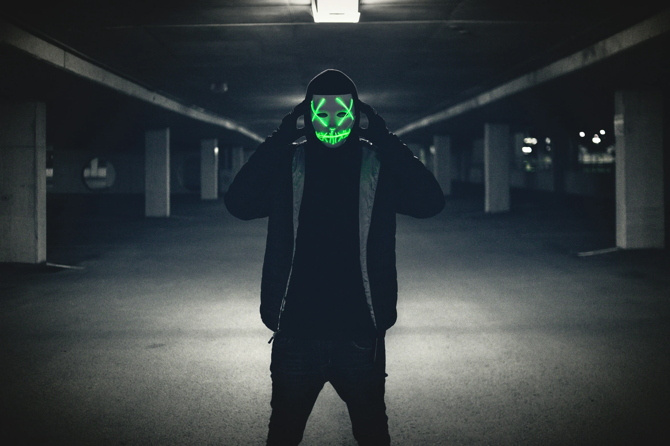 a man in an alien face mask and hood is standing under lights