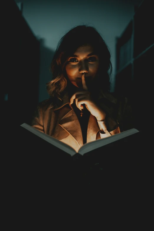 a woman in dark reading a book with a lit image over her face