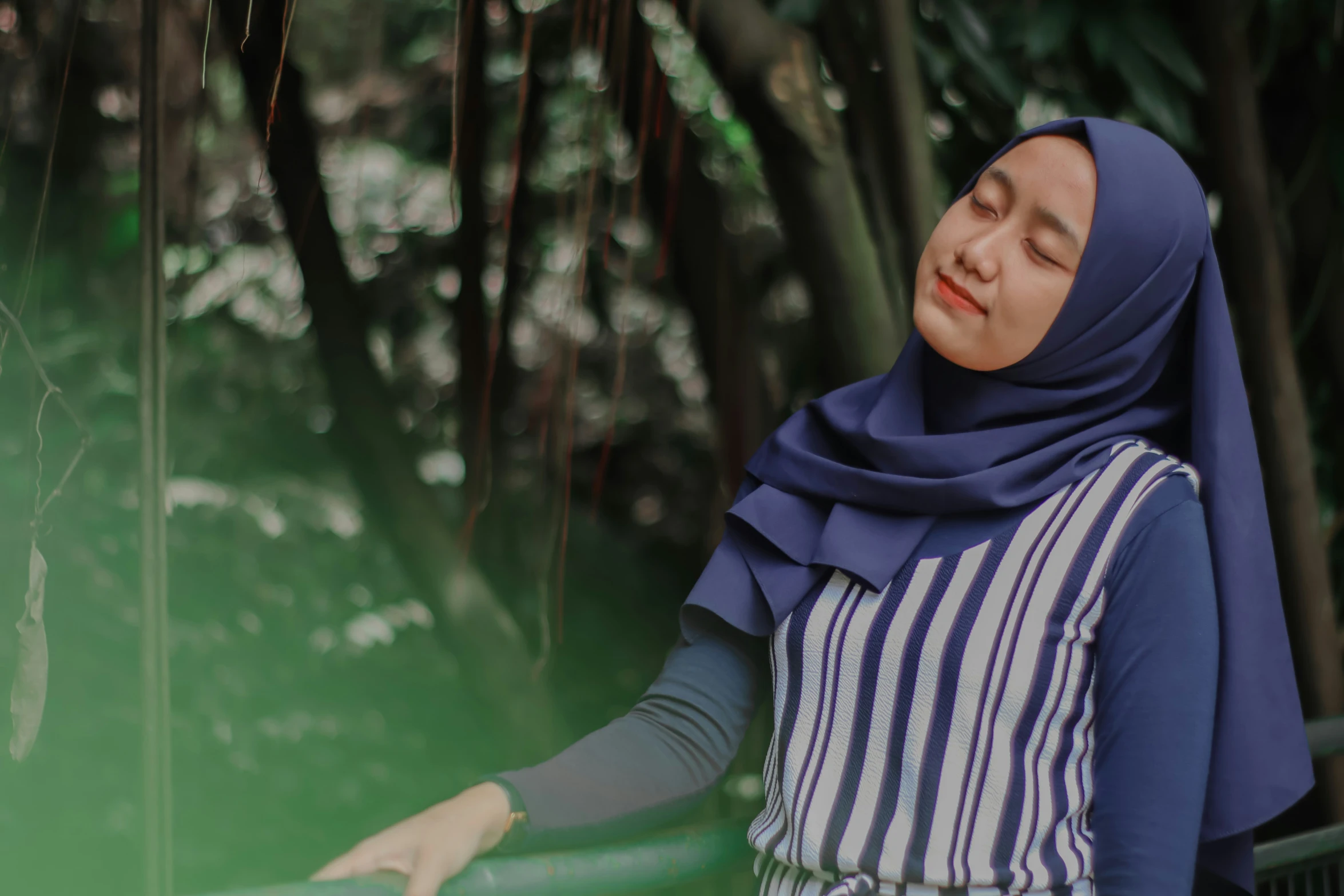 a woman standing near the trees with her head up