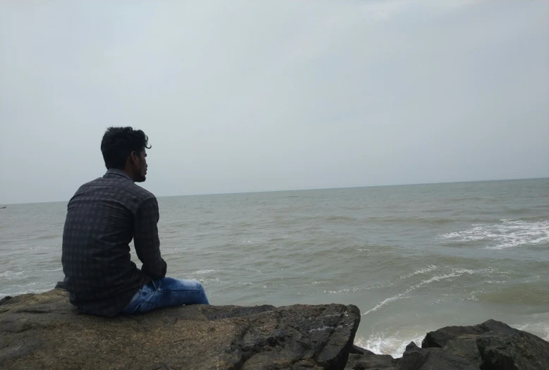 a man sits on rocks as he looks at the water