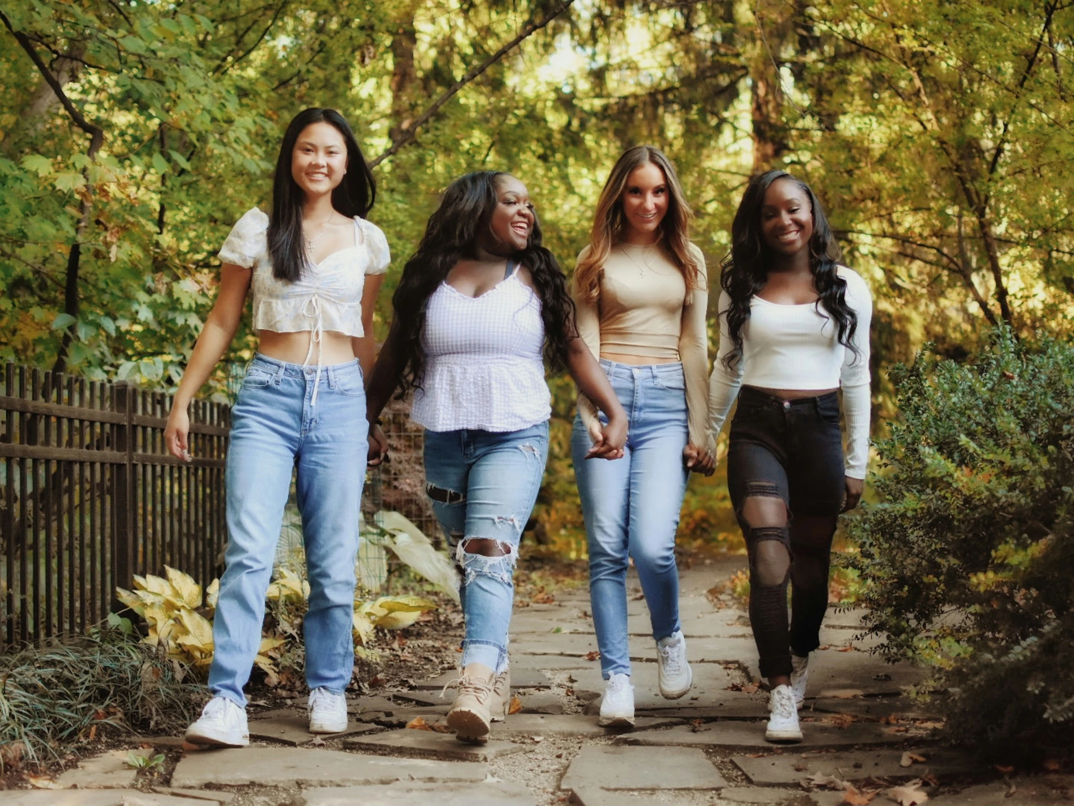 four beautiful women walking down a path next to a fence