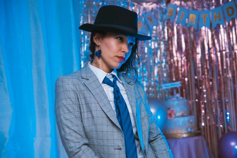 a woman in a suit and hat standing next to a blue backdrop