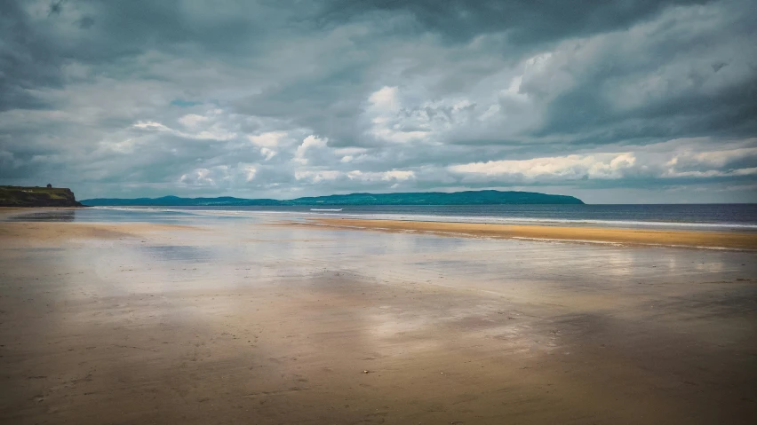 the ocean shore with clouds and a beach