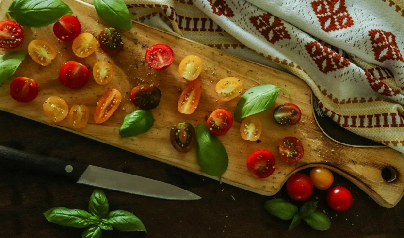 several tomatoes and basil are sliced on a  board