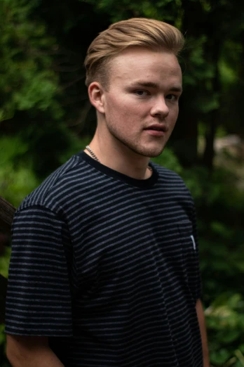 a boy stands outside in the woods wearing a black and grey  shirt