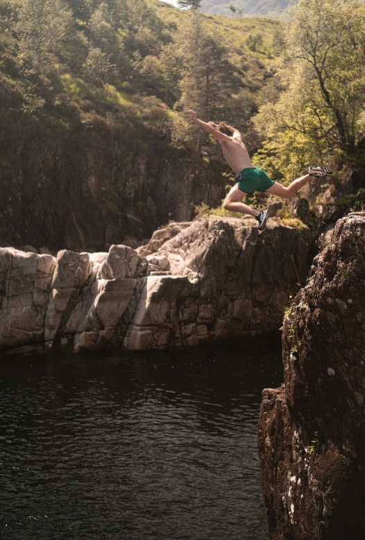 man wearing swimming trunks doing a diving trick off a cliff