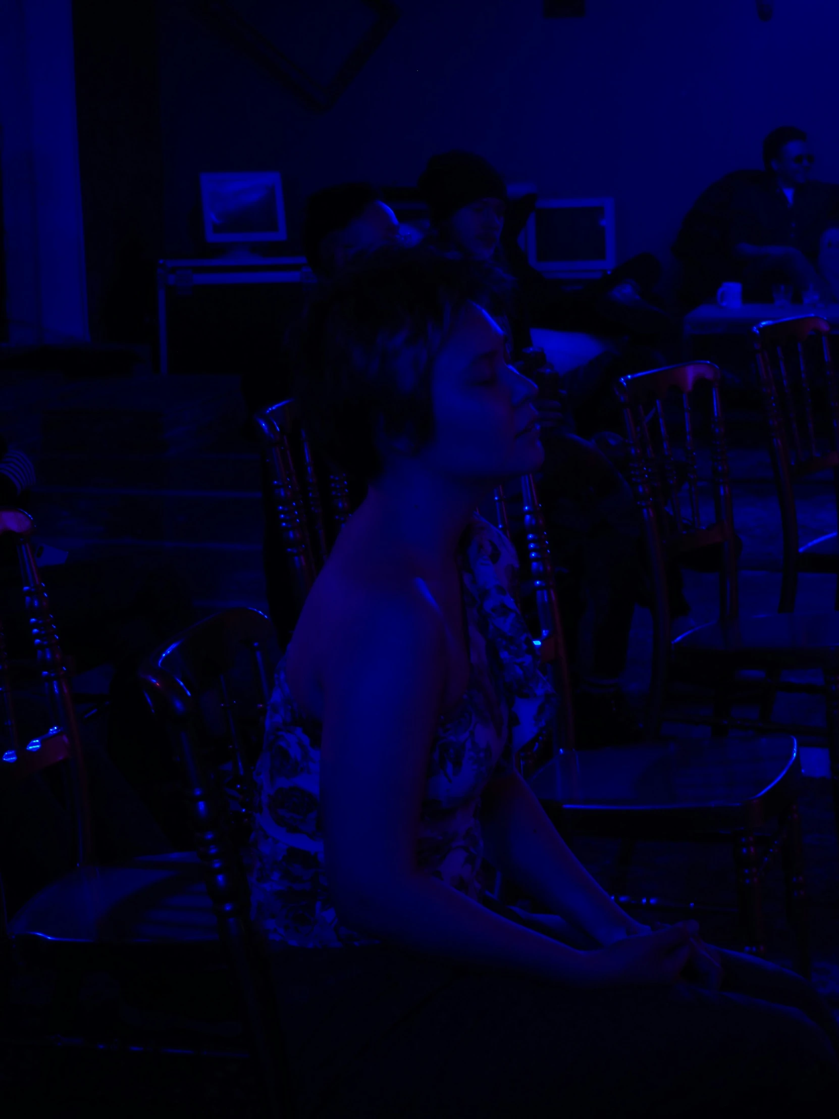 a person sitting in a dark room with chairs and a tv screen