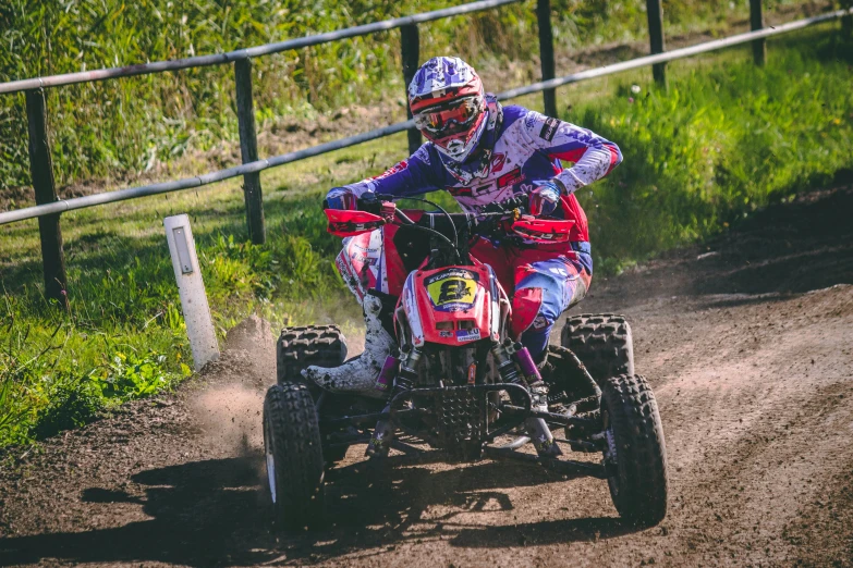 a man riding on the back of a red four - wheeler down a dirt road