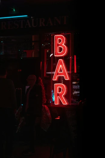 an illuminated bar sign in the dark with people