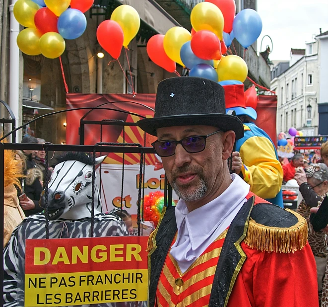 a man wearing a red and yellow striped top hat and an orange and white shirt holds up a sign