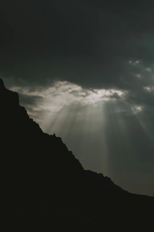 a silhouette of a hill with clouds and light from a sun ray