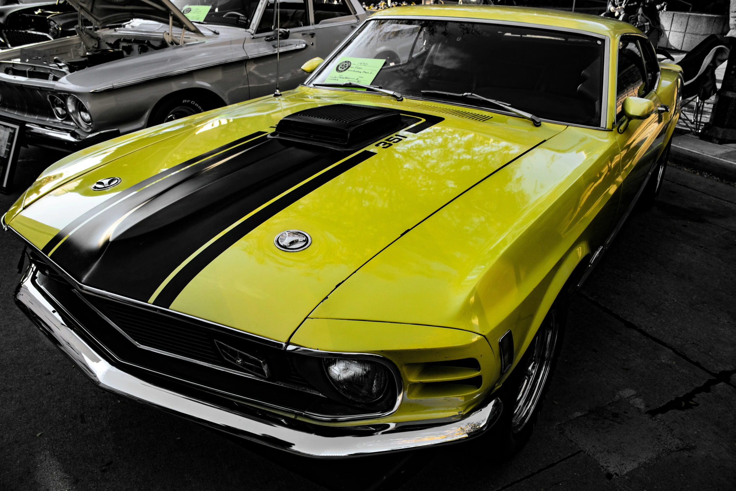 yellow mustang sits parked next to other cars