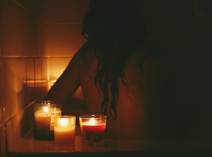 a woman sitting in front of candles with her arms on the counter