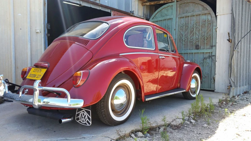 a large red volkswagen bug sitting outside of a garage