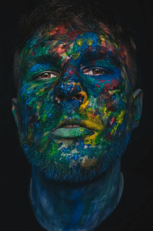 the man is covered in colored paint and looking into the camera