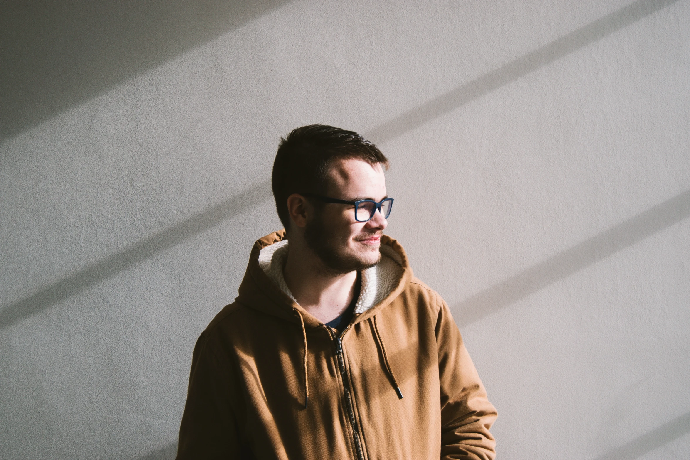 a man with glasses standing by a wall