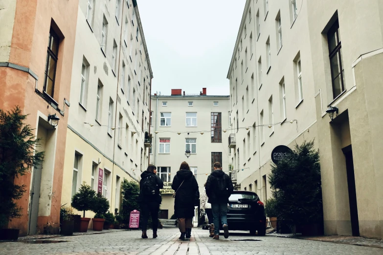 people walk down a narrow city street surrounded by tall buildings