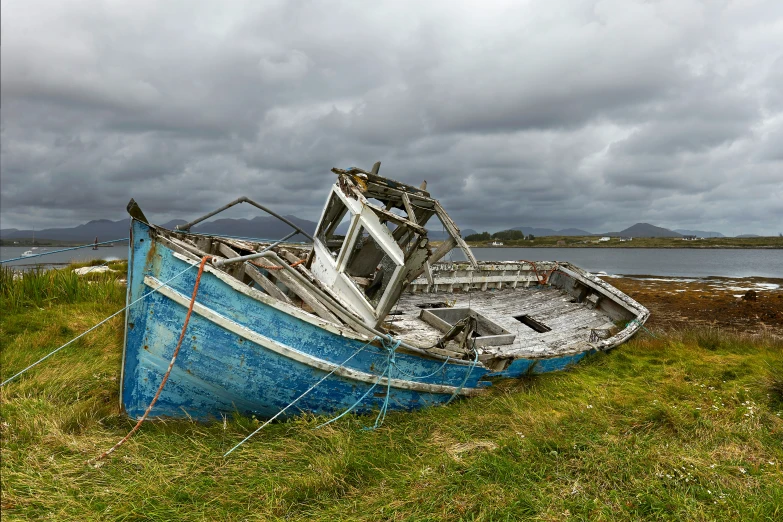 a boat in the grass next to water with cloudy skies