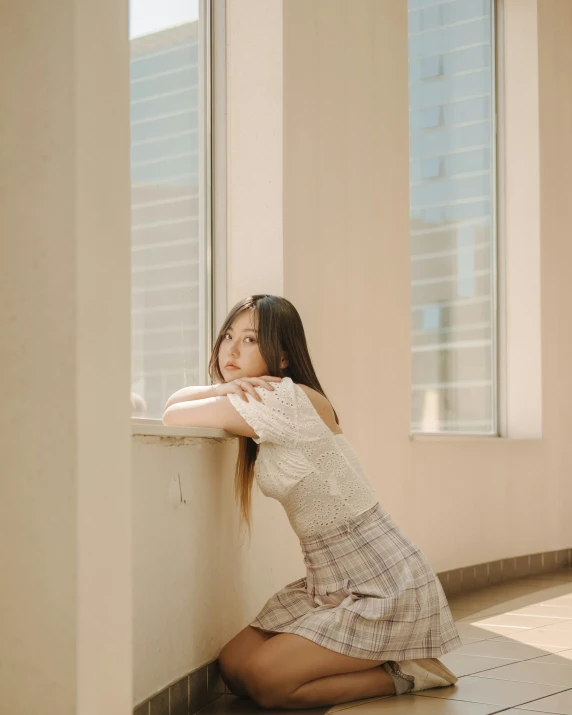 a beautiful young woman sitting by a window looking at the camera