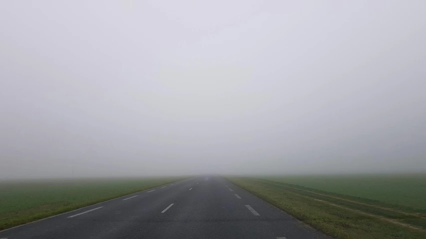 a foggy highway with green fields and a single plane in the distance