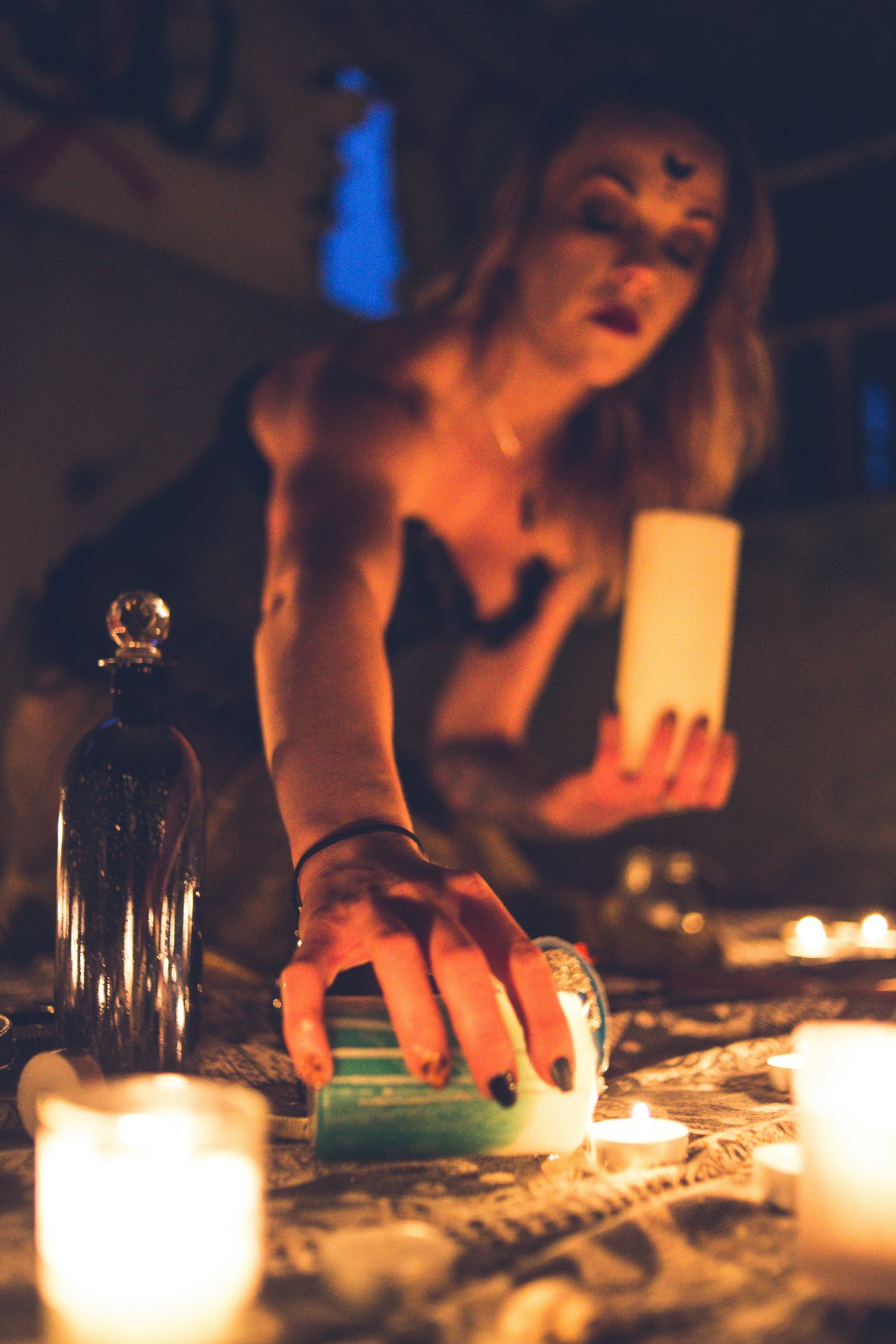 woman sitting on bed next to candles and a bottle