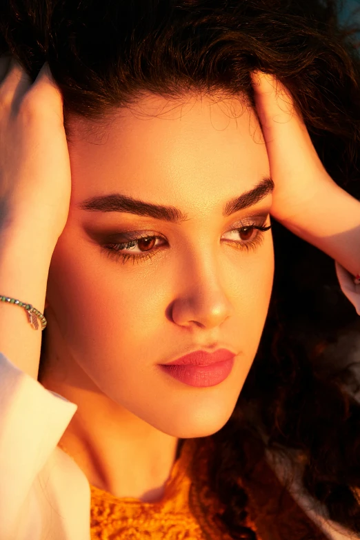 a young lady with black hair and make up, her hand on her head, a celet and some necklaces on her shoulder