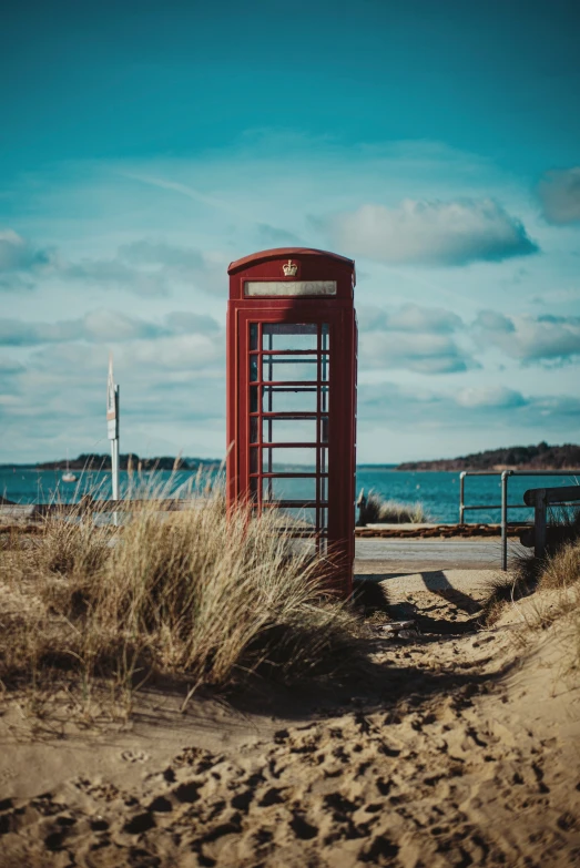 a phone booth sitting on top of sand near the water