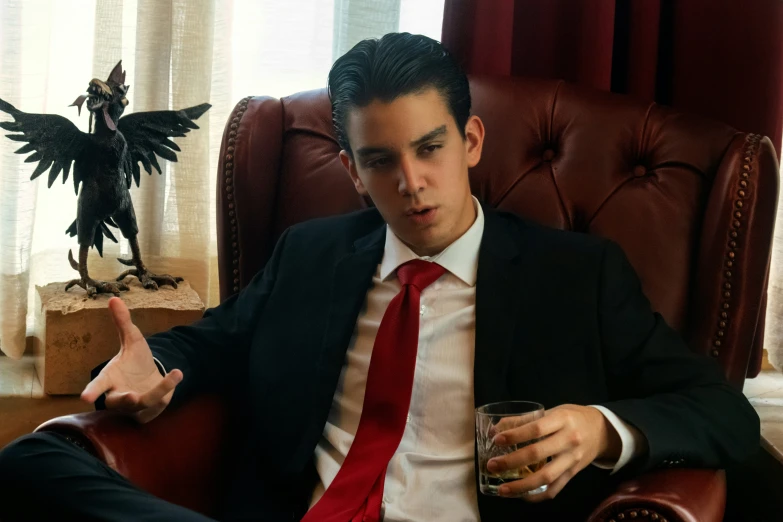 a young man in a business suit and red tie sitting next to a statue