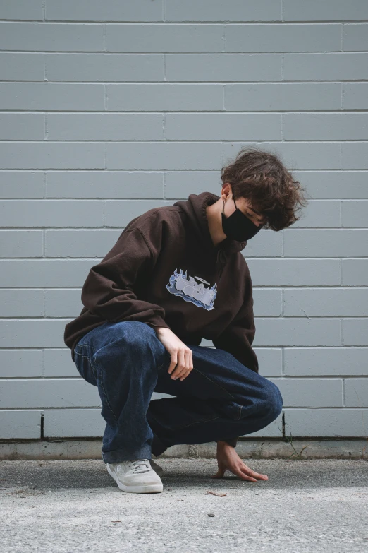 a young man with face mask squatting down on concrete