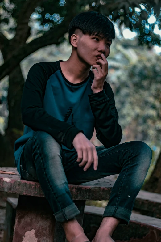 a young man smoking a cigarette as he sits on a wooden bench