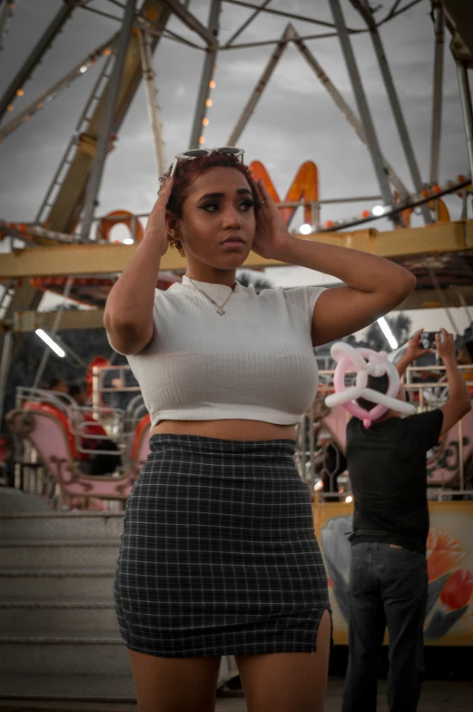 woman in plaid skirt covering her eyes standing in front of ferris wheel