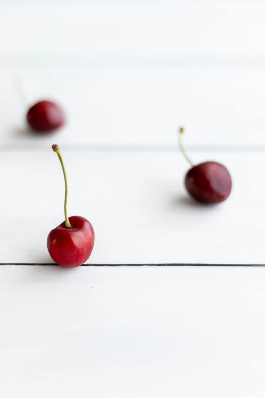 two cherries on the white surface with a single piece in the middle