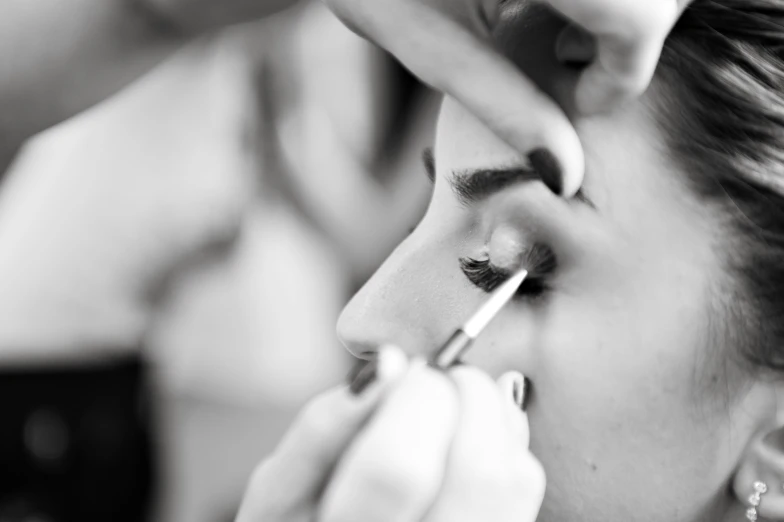 woman applying mascara on man's eye with other woman nearby