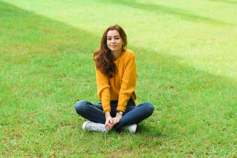 a woman sitting in the grass wearing a yellow shirt