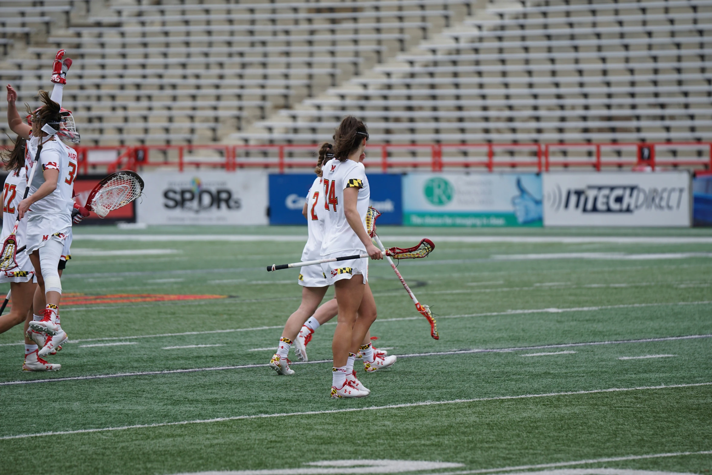several girls playing lacrosse on a field, in a stadium