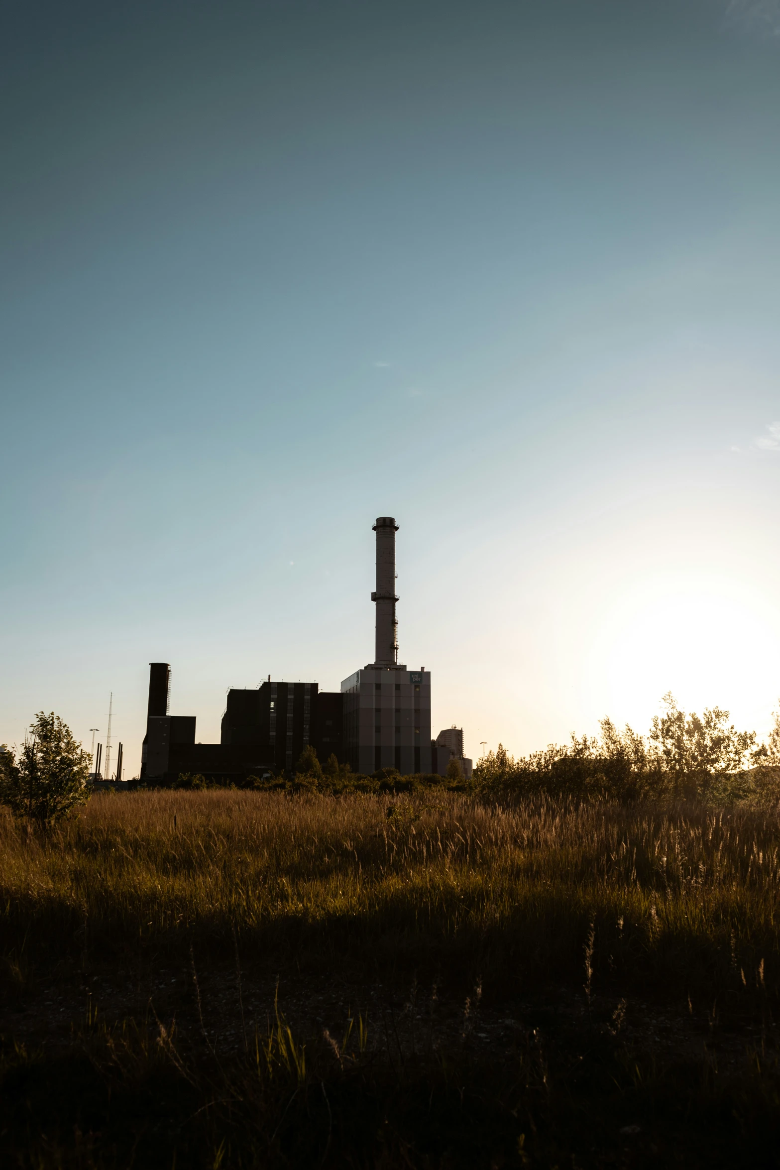 the silhouette of a factory building against a bright blue sky