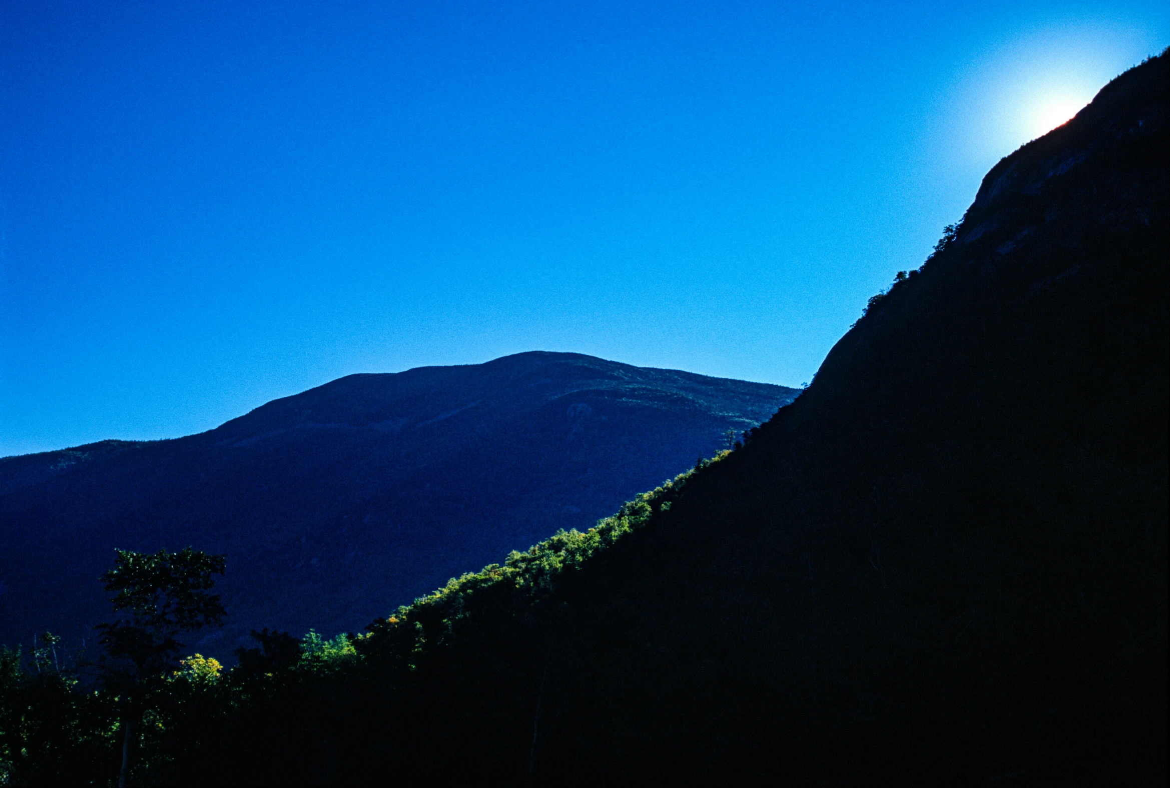 the sun shining over a mountain and a tree line