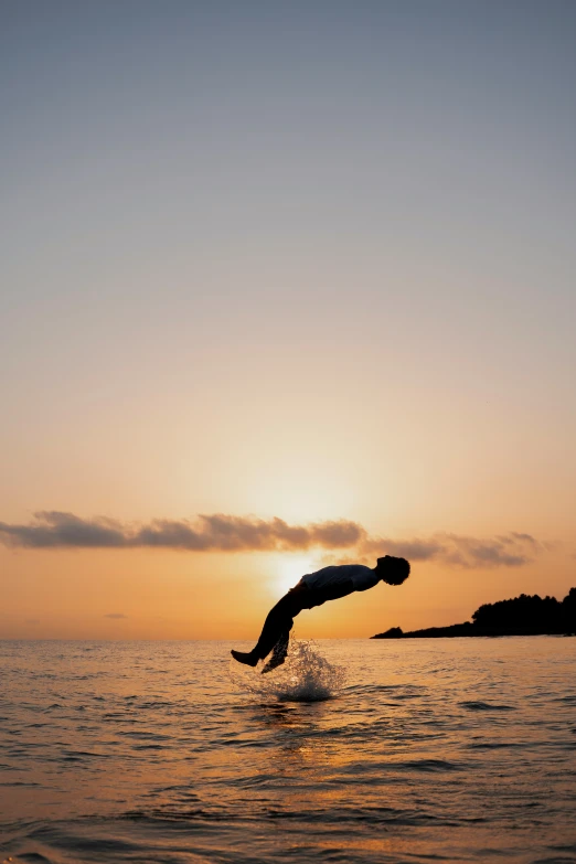 a person jumping in the air above water at sunset