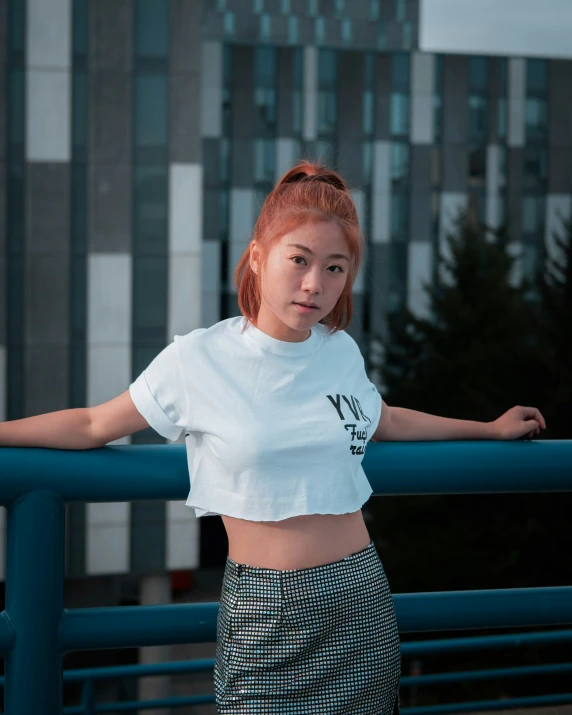 a woman in a white t shirt is leaning on the fence