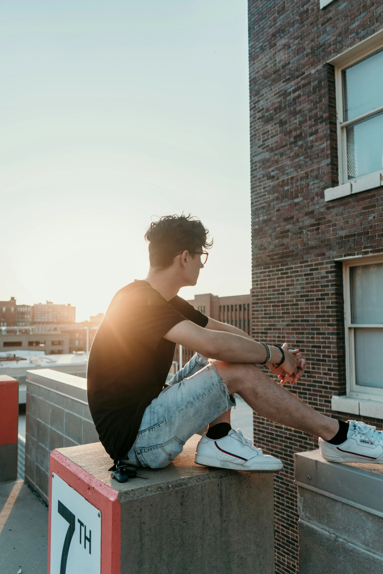 a young man wearing glasses sits on a cement slab