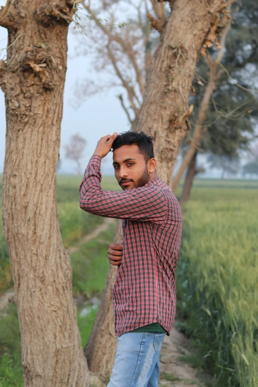 a man wearing jeans stands next to trees