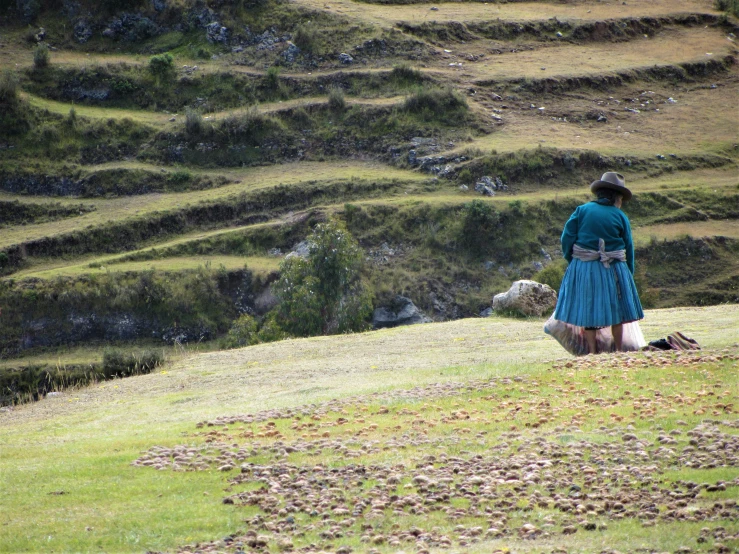 a woman in a dress walking her dog on a hill