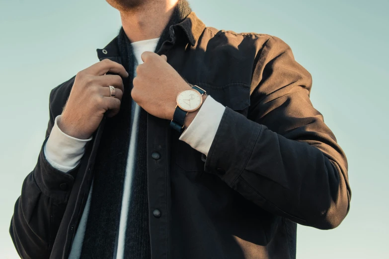 a man holding onto his watch while standing in front of blue skies