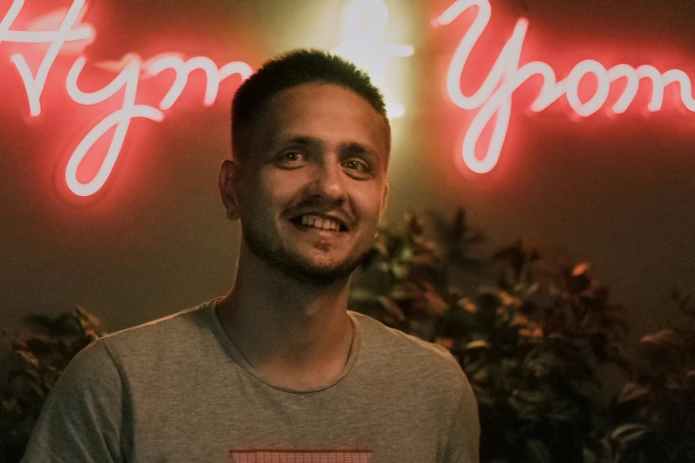 a man in gray shirt standing in front of a neon sign