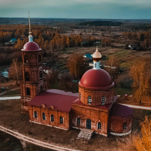 an old brick church sits on an unpaved field in autumn