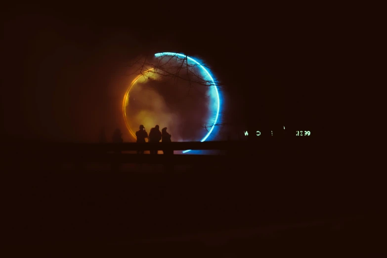 two people stand under an illuminated wheel on a dark night